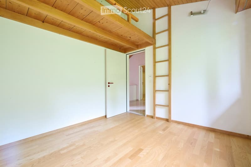 Empty room with light wooden flooring, white walls, and a wooden loft area accessible by a ladder. A closed door leads to another room with pink walls.