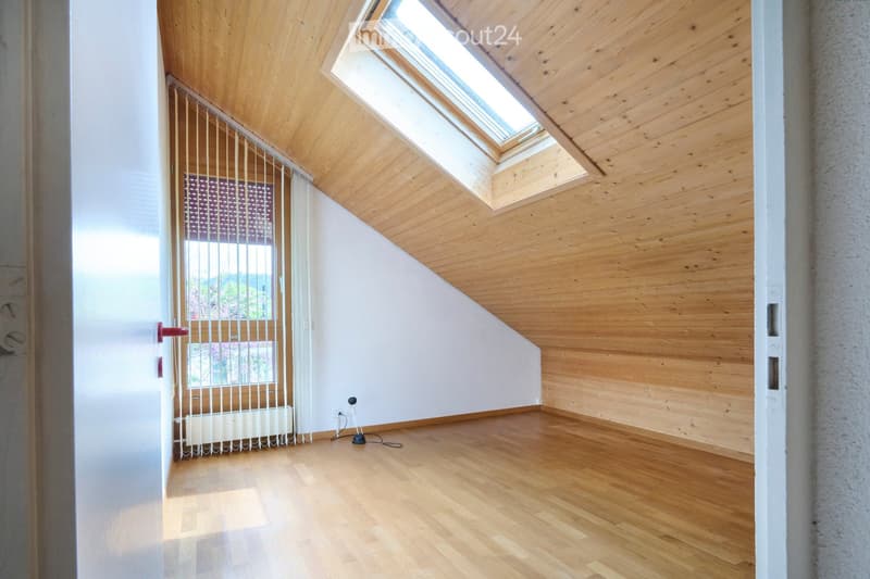 Empty attic room with wooden ceiling, wooden floor, skylight windows, and a radiator. No furniture or equipment present.