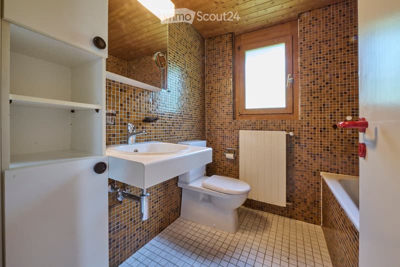 Bathroom with a white sink, toilet, bathtub, and wooden ceiling. Features mosaic tiles on walls and a window for natural light.