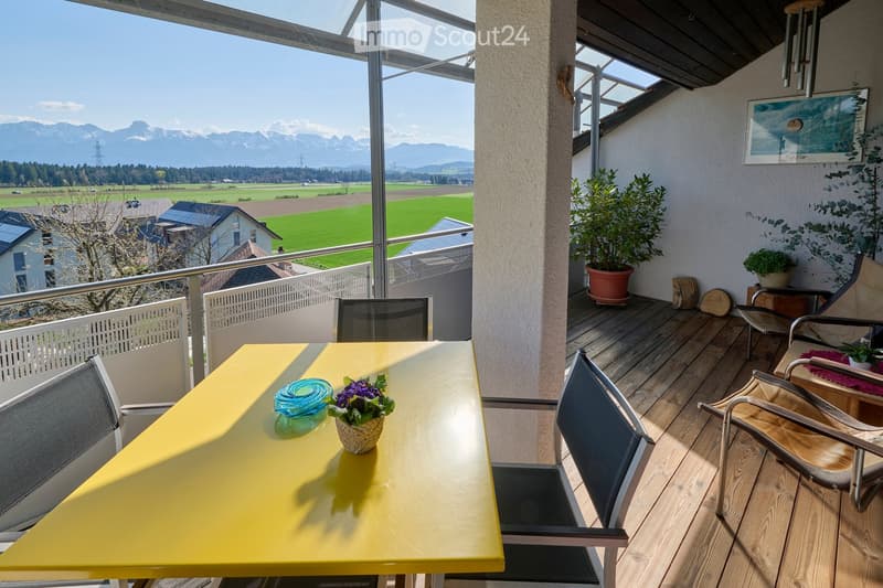 Balcony with wooden decking, yellow table, chairs, potted plants, and scenic mountain view.