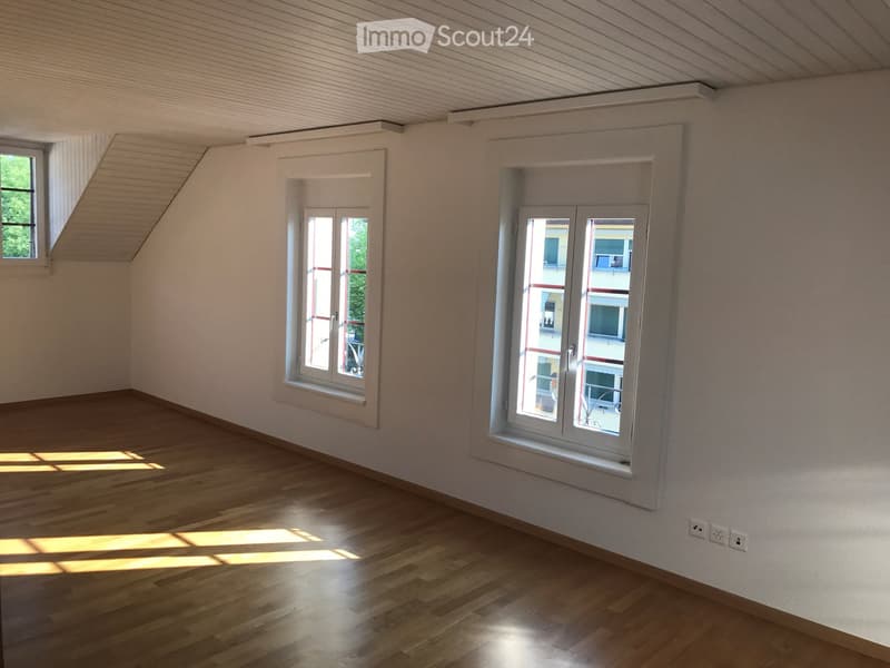 Empty room with wooden flooring, white walls, and multiple windows allowing natural light to enter.