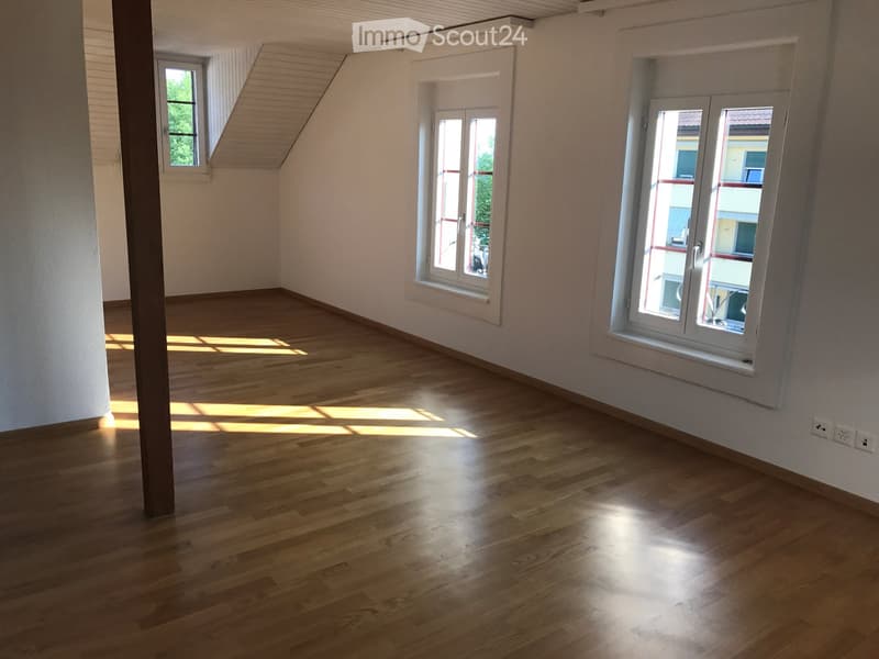 Empty room with wooden flooring, white walls, and multiple windows allowing natural light to enter.