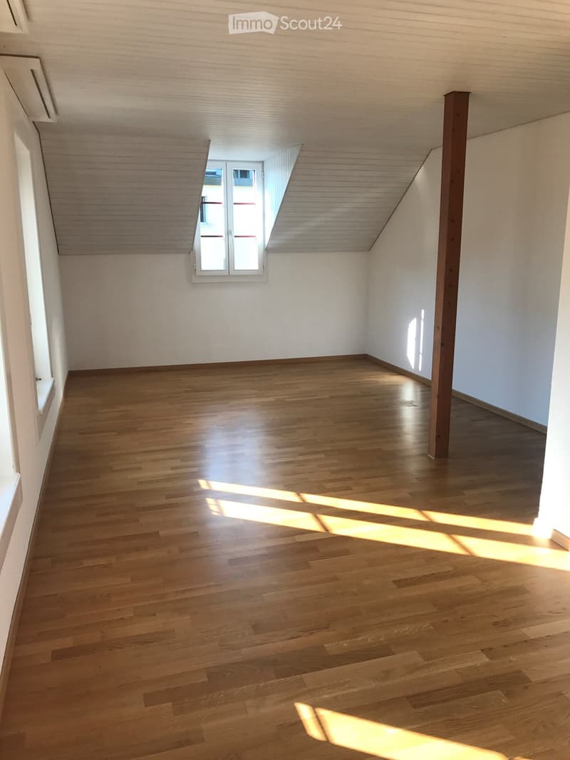 Empty room with wooden flooring, white walls, and a skylight window allowing natural light to enter.