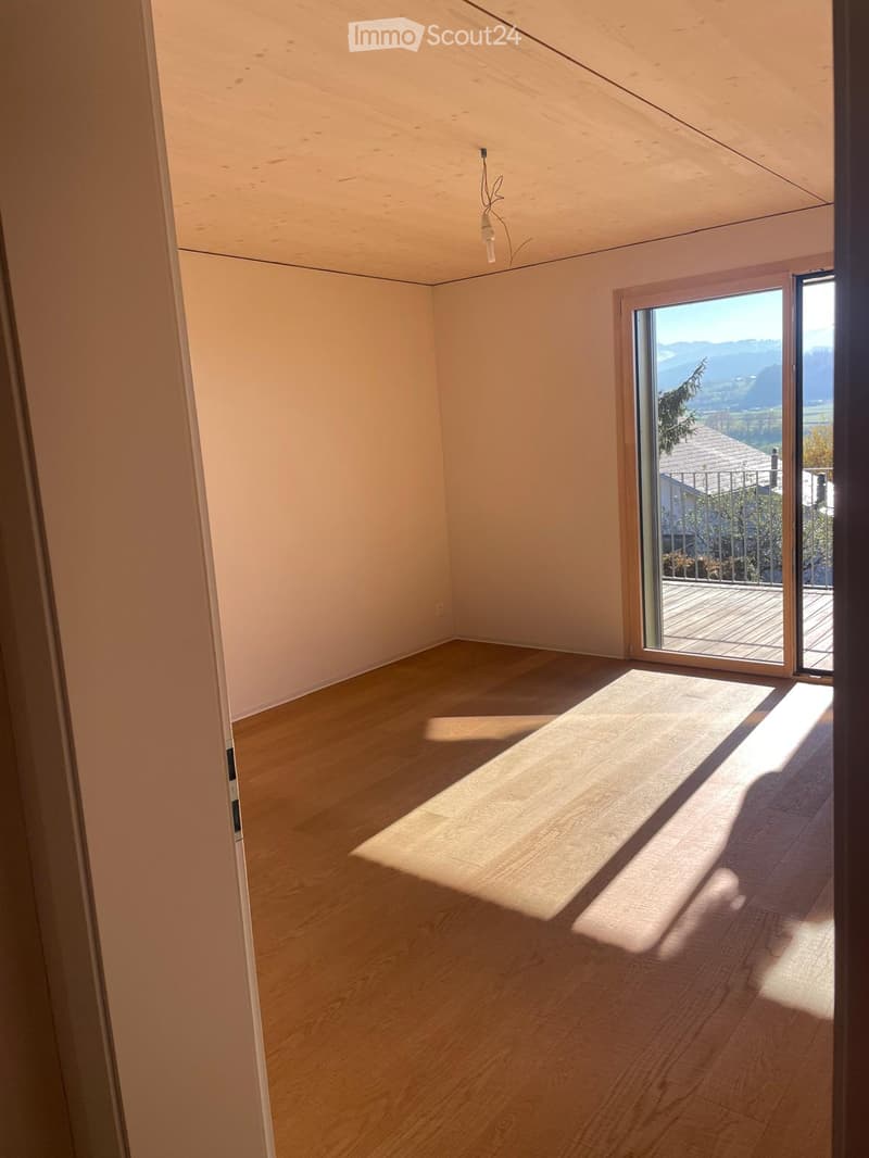 Empty room with light wooden flooring and white walls, featuring a large sliding glass door leading to a balcony with a scenic mountain view.