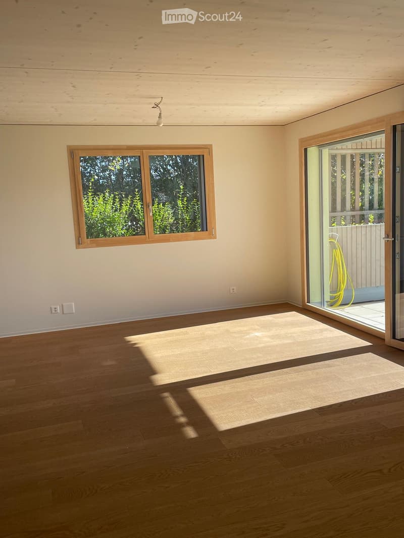 Empty room with wooden flooring, large windows, and a sliding glass door leading to an outdoor area.