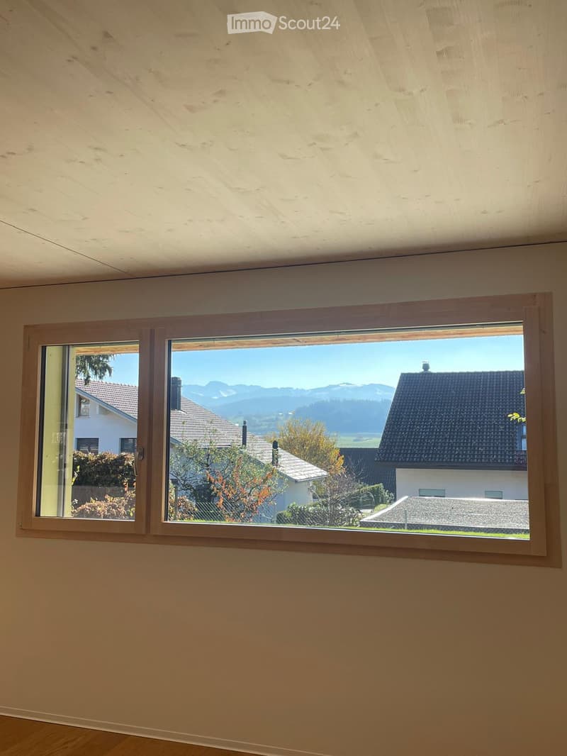 Empty room with wooden floor and large window offering a scenic mountain view.