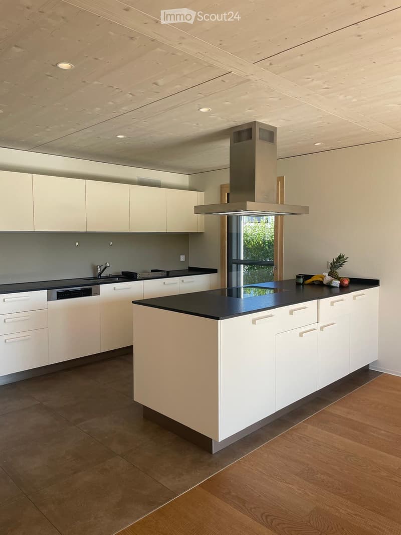 Modern kitchen with white cabinets, black countertops, island, range hood, and sink.