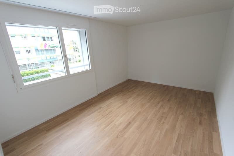 Empty room with wooden flooring and white walls, featuring large windows with a view of the outside area.