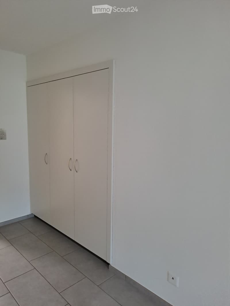 Empty room with white walls and tiled floor. A large white closet with two doors is against the wall. A power outlet is visible on the right wall.