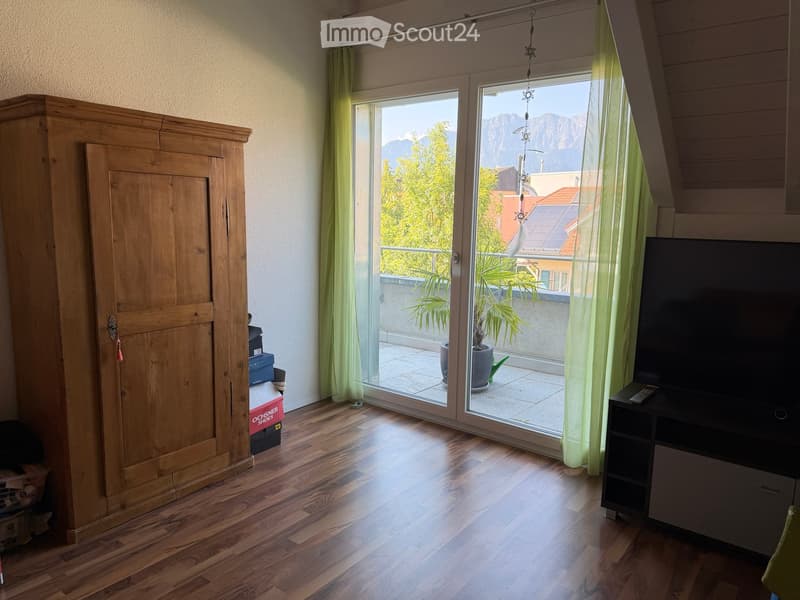 Bright room with wooden flooring, large window offering a scenic mountain view, wardrobe, TV stand, and remote control on the stand.