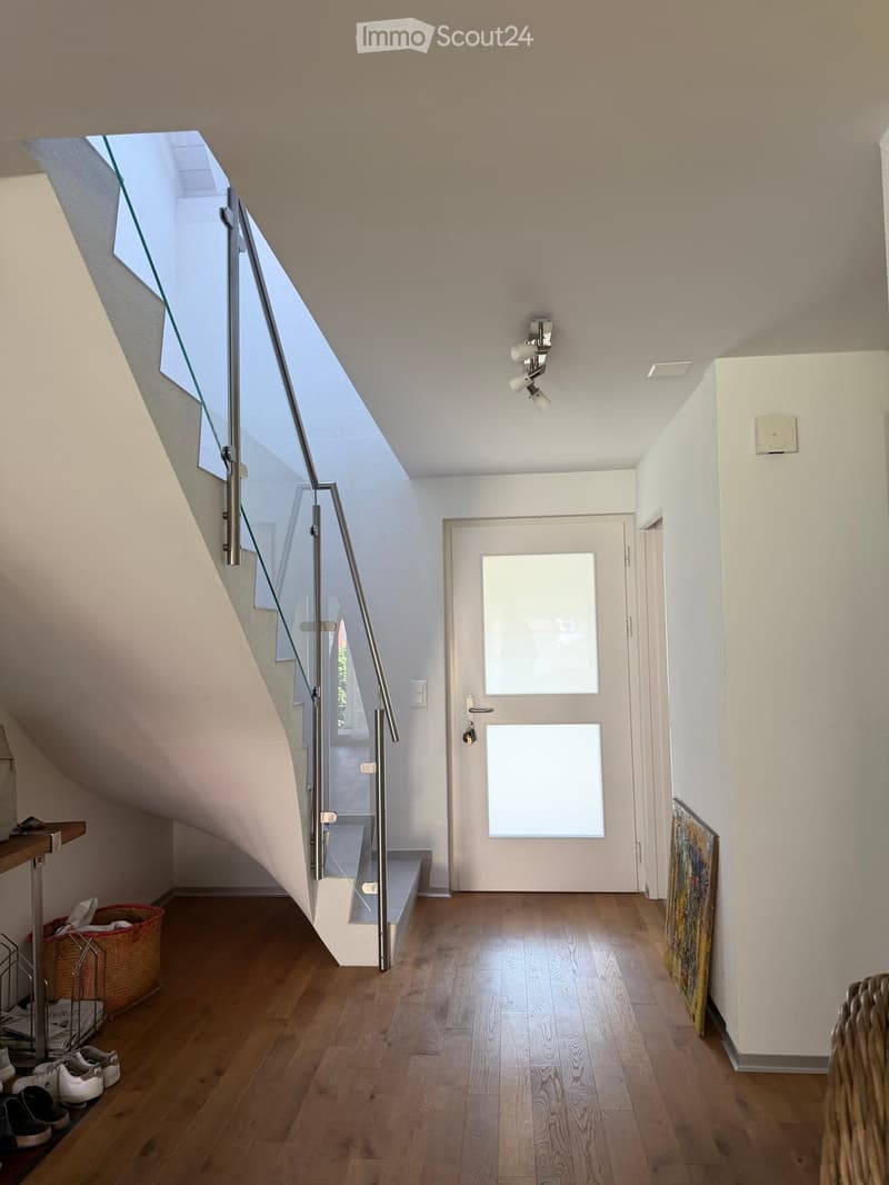 Modern hallway with wooden flooring, glass staircase railing, recessed lighting, and a white door with frosted glass panels.