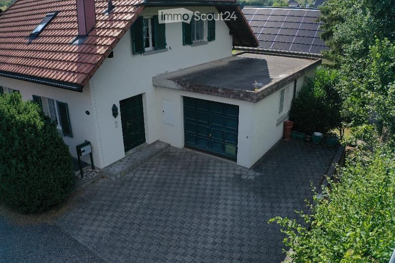 Two-story house with a red-tiled roof, white exterior, green shutters, and a large garage. Solar panels on the roof of an adjacent structure.