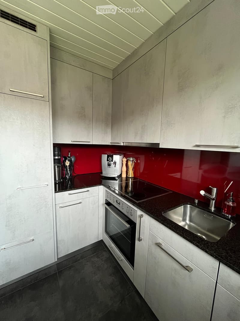 Modern kitchen with white cabinets, dark countertops, stainless steel sink, coffee maker, and built-in oven.