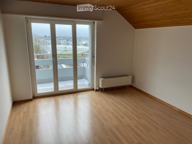 Empty room with wooden flooring, large sliding glass doors leading to a balcony, and a radiator on the wall.