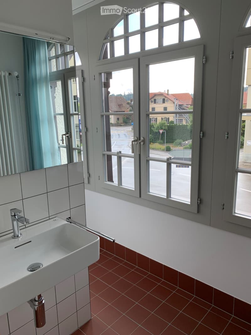 Modern bathroom with white tiled walls, red tiled floor, large windows, and a white sink with a chrome faucet.
