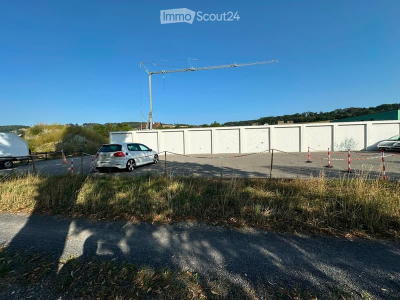 Outdoor parking area with multiple garage units, a silver car, and a construction crane in the background.