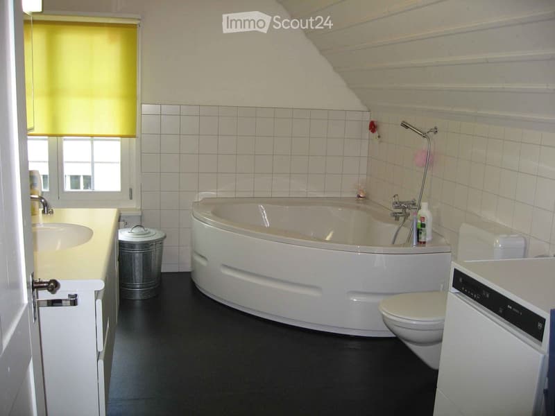 Bathroom with a bathtub, toilet, sink, and a window with blinds. The room features white tiled walls and a black floor.
