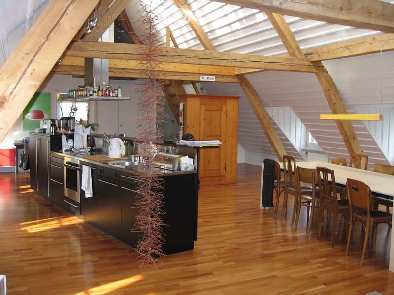 Open-plan kitchen and dining area with wooden beams, modern appliances, and a central island. The kitchen features stainless steel appliances, wooden cabinets, and a dining table with chairs.
