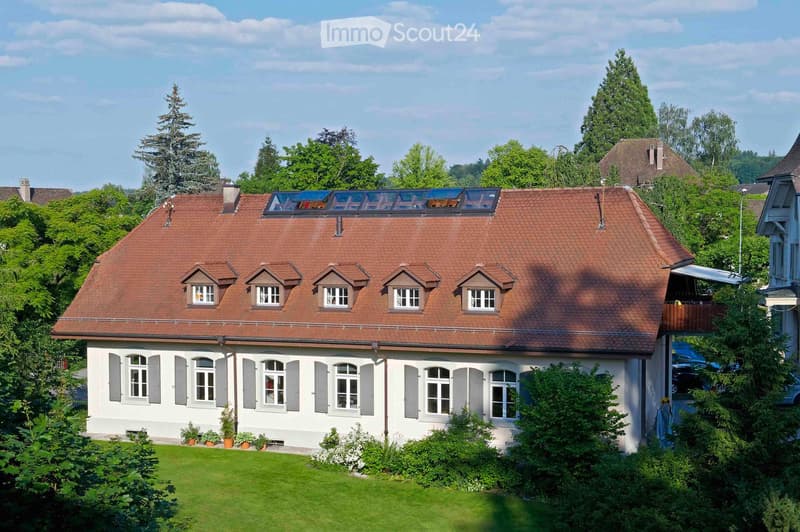 Two-story house with red-tiled roof, multiple dormer windows, white siding, and a well-maintained garden.