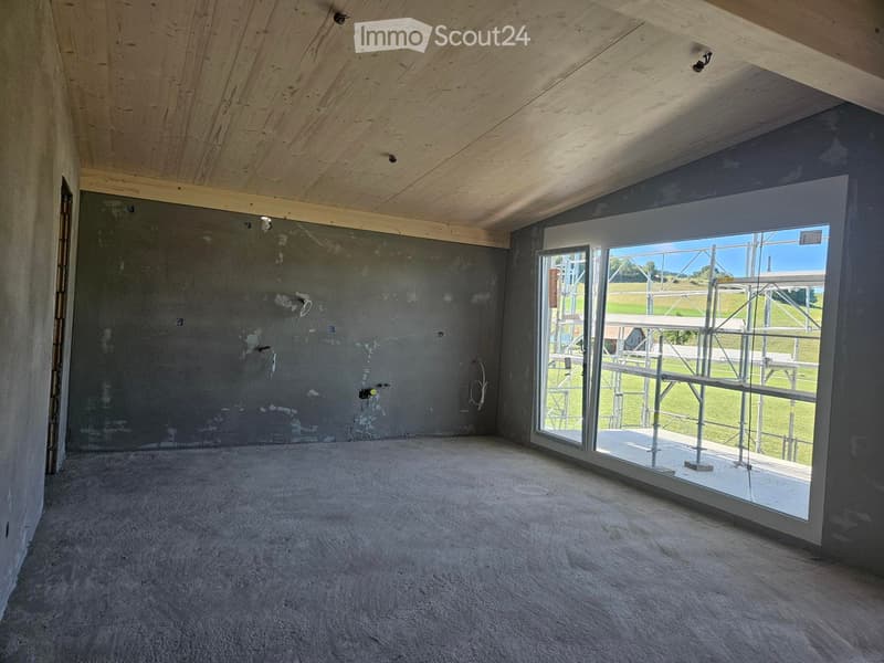 Empty room with exposed wooden ceiling, unfinished concrete walls, and large glass door leading to outdoor area.