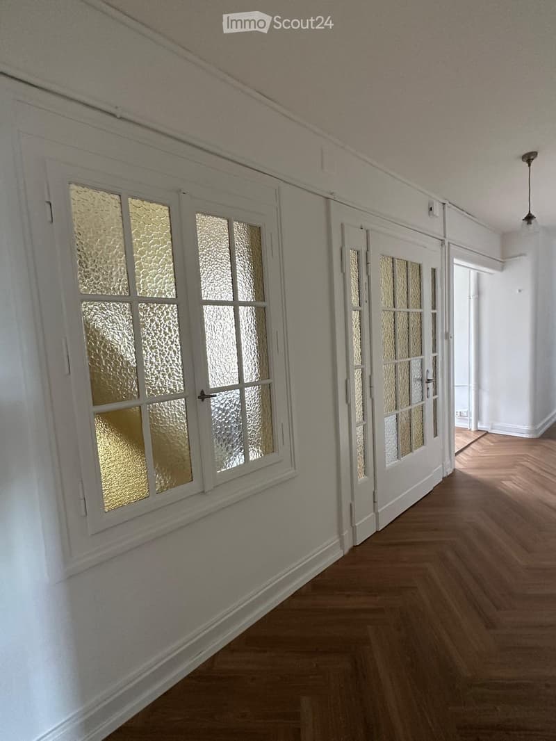 Empty hallway with wooden flooring, white walls, and frosted glass doors leading to other rooms.