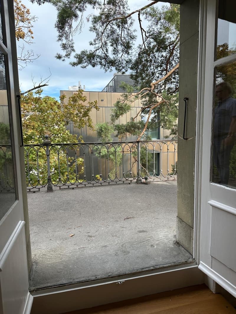 Balcony with metal railing, concrete floor, and view of trees and buildings.
