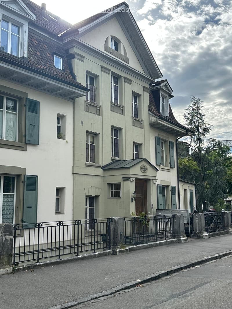 Two-story house with light green facade, multiple windows, shutters, and a small entrance gate.