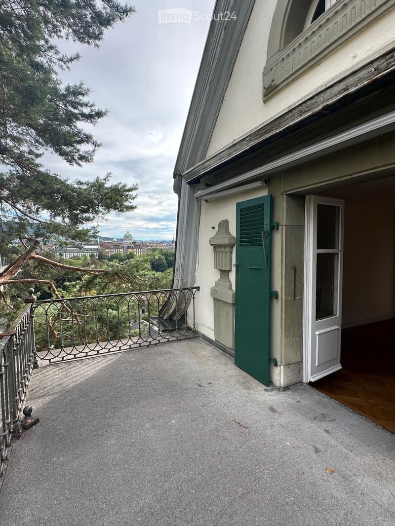 Balcony with metal railing, green shutters, and a view of the city and trees.