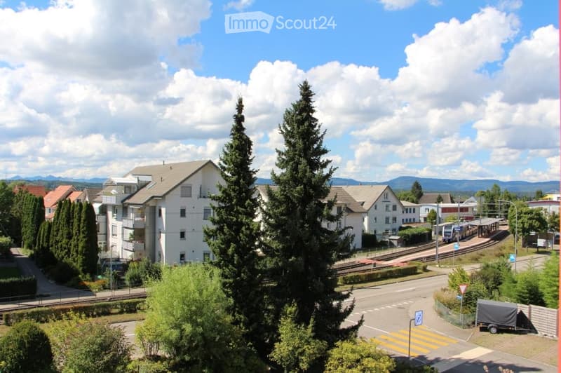 A view of a suburban neighborhood with houses, trees, a train track, and a clear blue sky with scattered clouds.