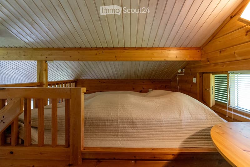 Bedroom. Cozy wooden loft bedroom with slanted ceilings, a large bed, and a small table near the window.