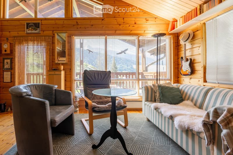 Furnished Room. Cozy living room with wooden walls, large windows, a sofa, armchair, coffee table, floor lamp, and a guitar on the wall.