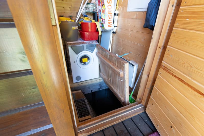 Bathroom. Small wooden-walled utility space with a washing machine, storage bins, and cleaning supplies.