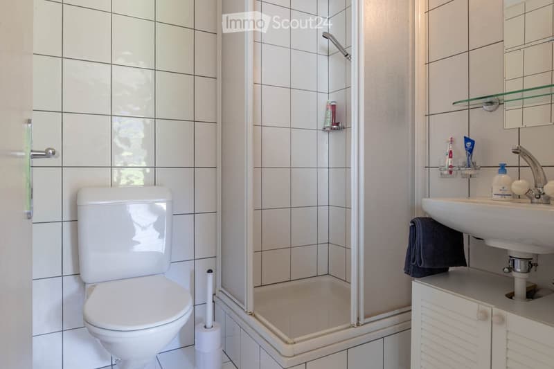 Bathroom. Modern bathroom with white tiles, a toilet, a sink with a mirror, a shower, and a towel on the counter.