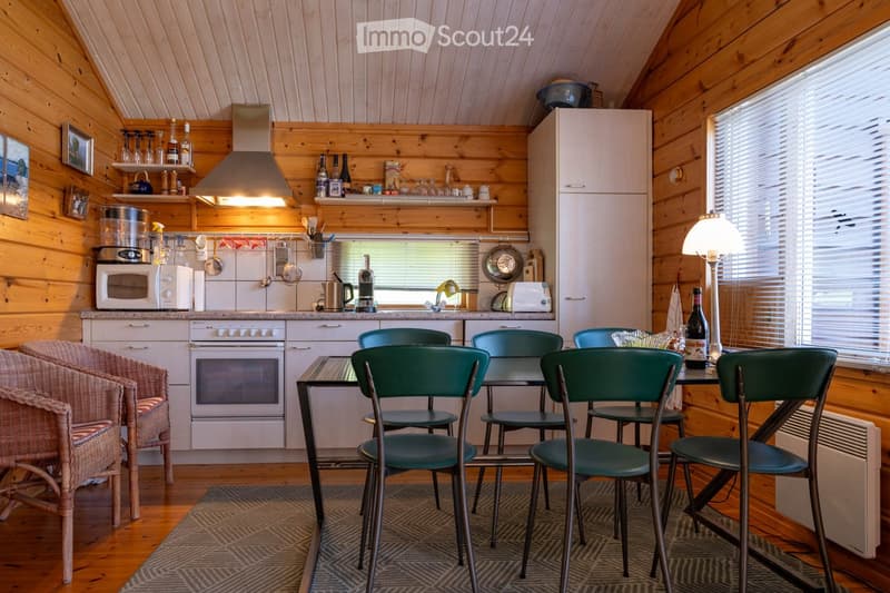 Kitchen. Cozy kitchen with wooden walls and ceiling, featuring a refrigerator, oven, microwave, coffee maker, dining table with chairs, and a wicker chair near the window.