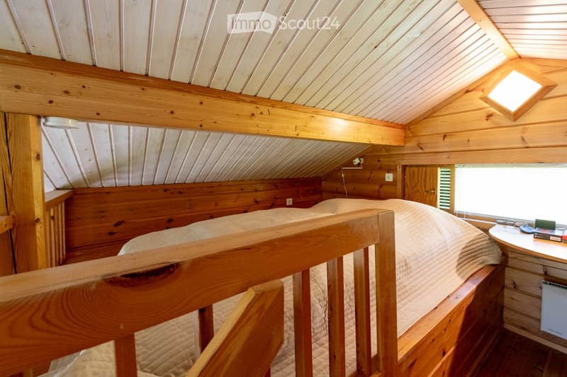 Bedroom. Cozy wooden loft bedroom with slanted ceilings, a double bed, a small nightstand, and a wooden railing.