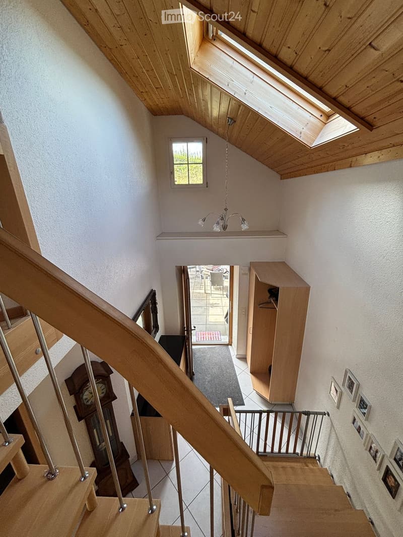 Spacious hallway with wooden staircase, skylight windows, and a chandelier. Features a grandfather clock, framed pictures, and a small closet.