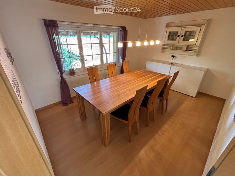 Bright dining room with wooden dining table and chairs, white cabinet, and large window with curtains.