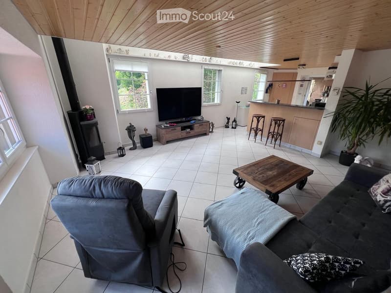 Living room with a grey sofa, coffee table, television, fireplace, and bar area with stools.