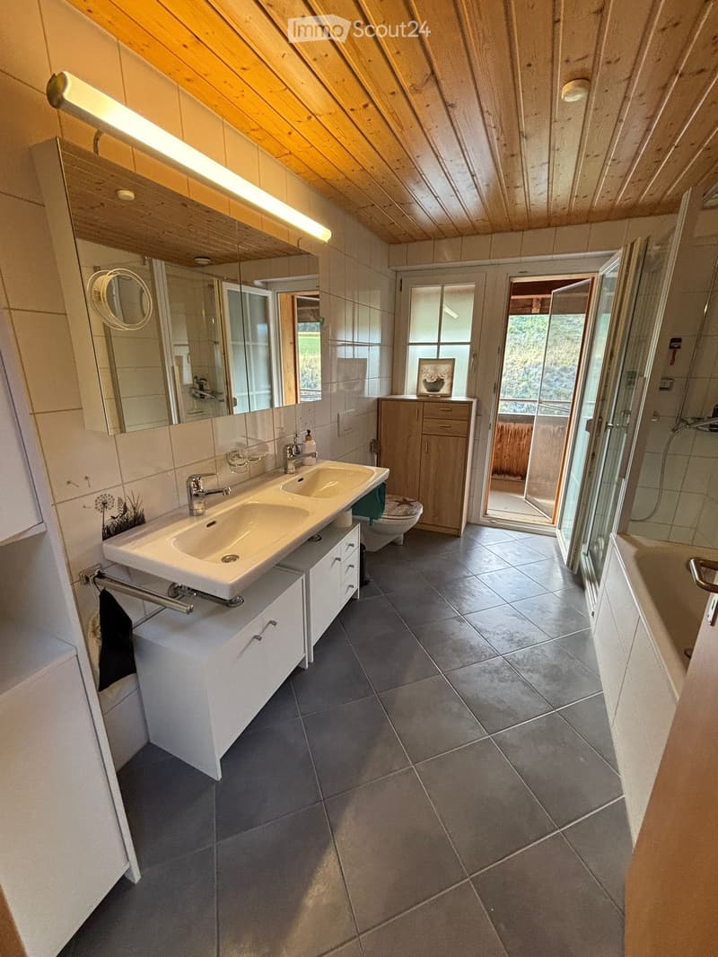 Modern bathroom with double sink, large mirror, wooden ceiling, tiled floor, and a separate shower area with glass enclosure.