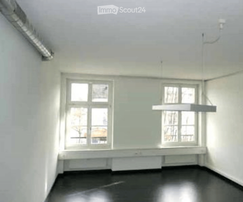 Completely empty room with white walls, dark flooring, and two windows with white frames. No furniture or equipment.