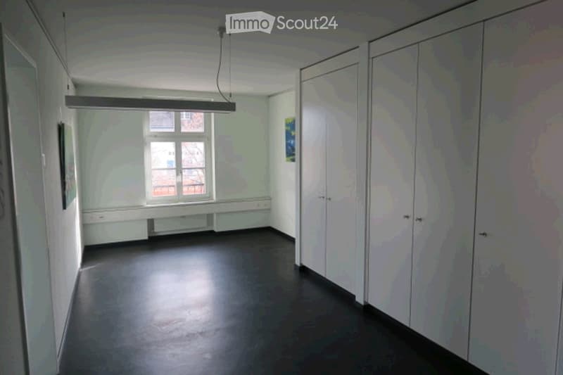 Empty room with white walls, dark flooring, large window, built-in cabinetry, and a hanging light fixture.