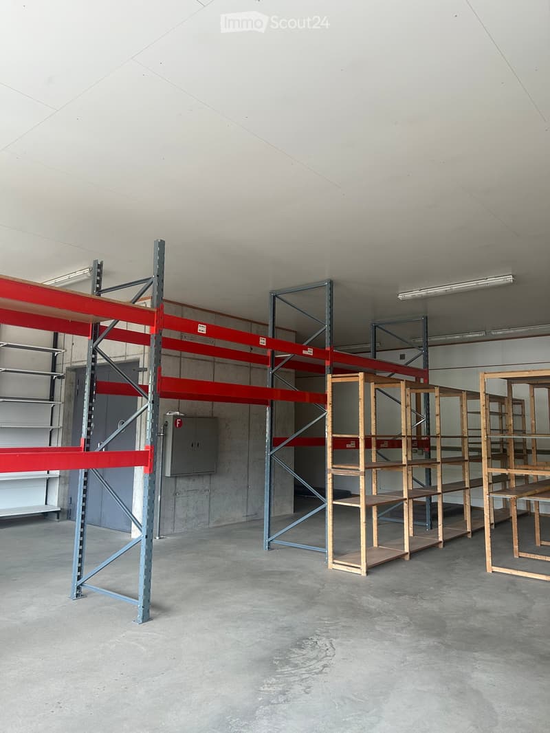 Empty warehouse space with concrete floors and walls, featuring metal shelving units and wooden shelving units.