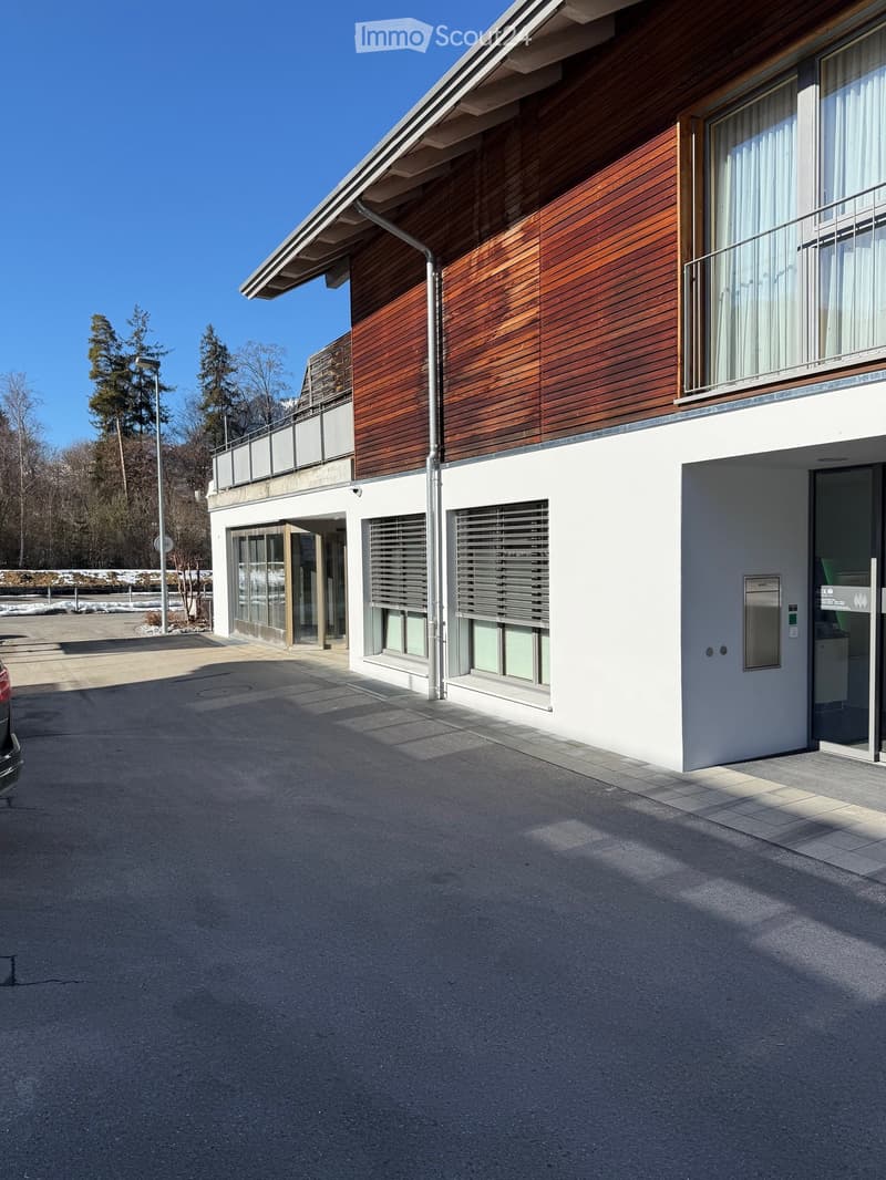 modern building with wooden facade, glass windows, raised ground floor, parking lot