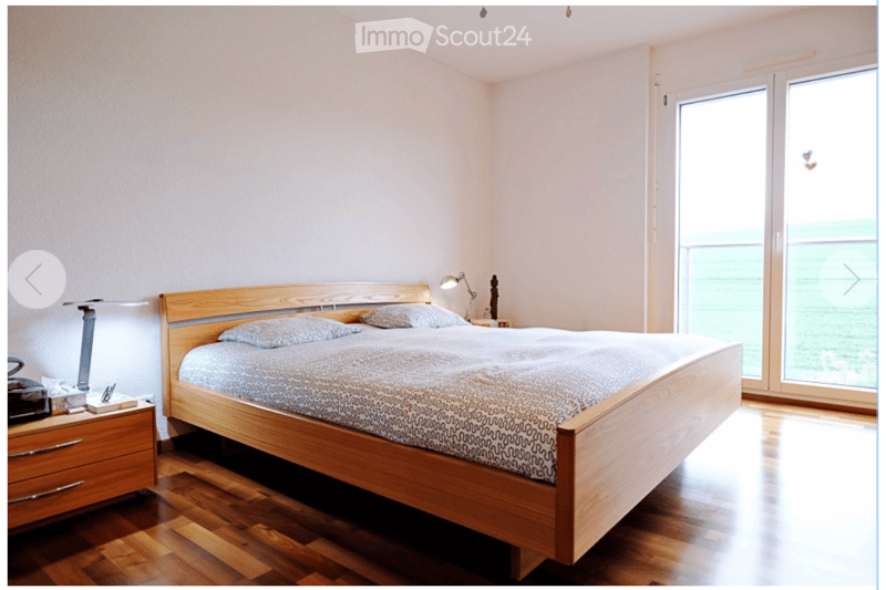 Modern bedroom with wooden bed, nightstand, and large window offering a view.