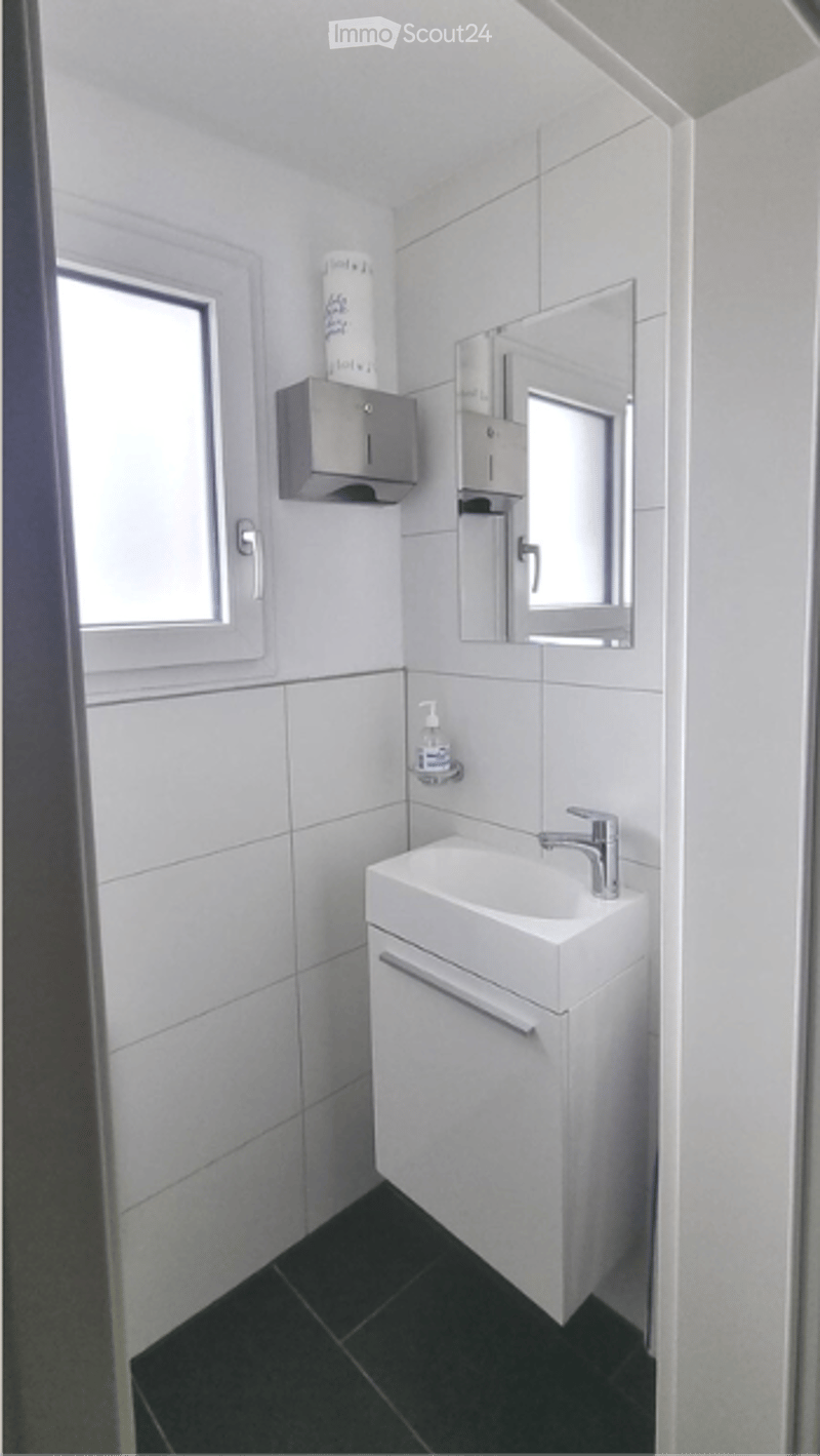 Modern, minimalist bathroom with white tiles, a white sink, a mirror, and a soap dispenser.