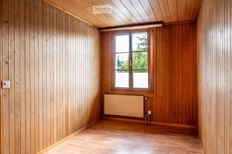 Empty room with wooden walls, ceiling, and floor, featuring a large window and a radiator.