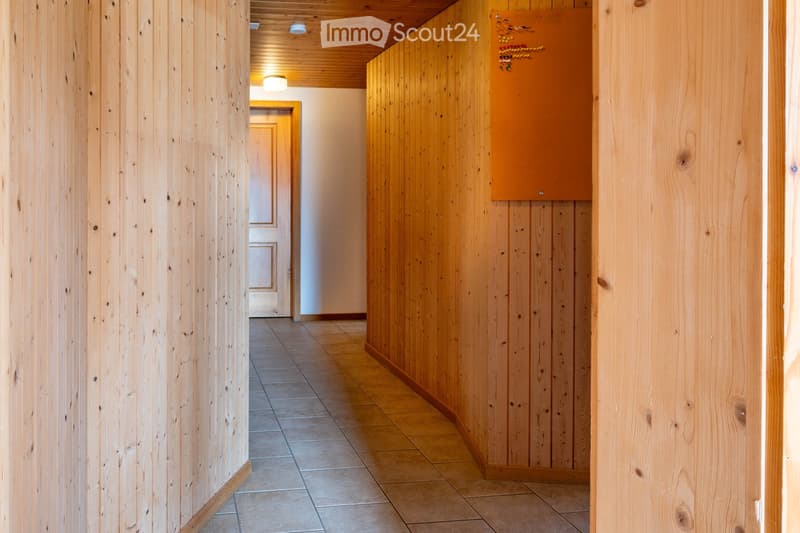 A narrow hallway with wooden panel walls and a tiled floor, featuring recessed lighting and a decorative wooden sign on the right wall.