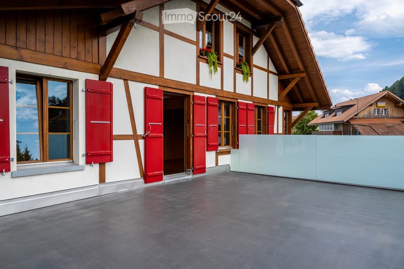 Traditional wooden-framed house with white walls, red shutters, and a spacious concrete patio area.