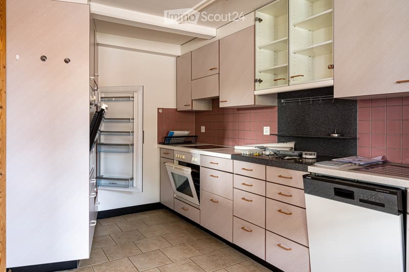 Modern kitchen with light wood cabinets, stainless steel appliances, and a tiled backsplash. Features include a refrigerator, oven, dishwasher, countertop, sink, and various kitchen items.