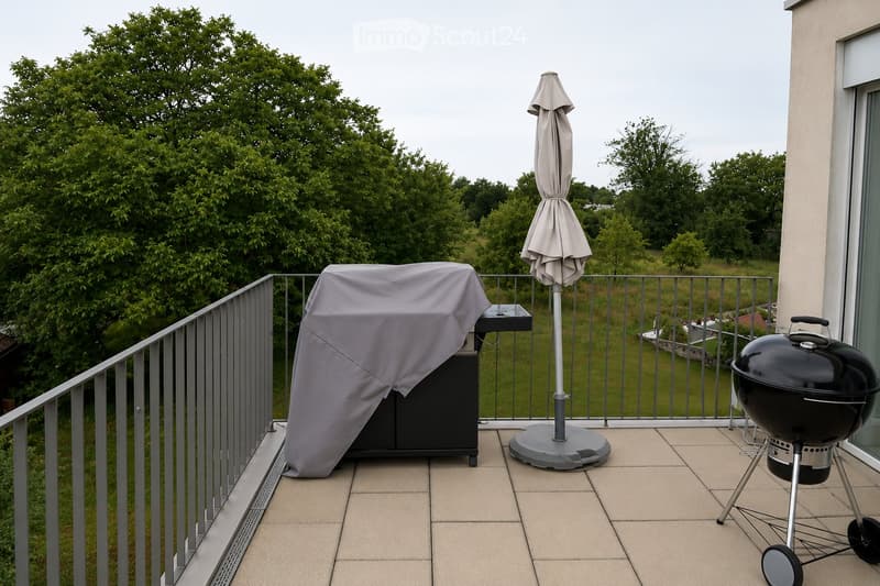 Balcony with a covered grill, a patio umbrella, and a railing overlooking a green landscape.